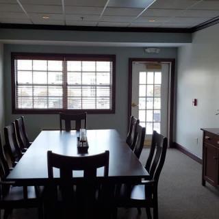 A conference room with a large table and chairs, featuring a window and door.