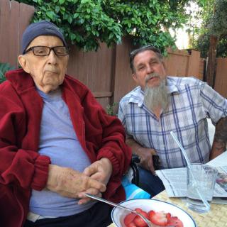 Two people sitting outdoors with a bowl of fruit on the table.