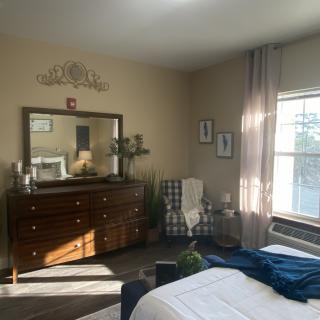 A cozy bedroom with a dresser and mirror, featuring a comfortable chair by the window.