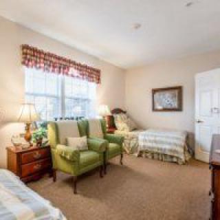 A cozy bedroom with two beds, green armchairs, and a window with natural light.