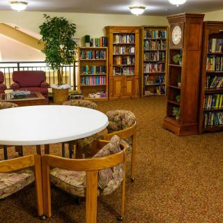 A cozy library reading area with bookshelves, a round table, and comfortable chairs.