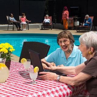 Seniors enjoying a leisurely afternoon by the pool, sharing laughter and drinks at a checkered table.
