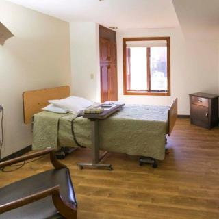 A hospital room with a bed, wooden floor, and a window providing natural light.