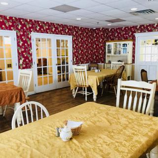 A cozy dining room with tables and chairs, featuring red floral wallpaper.