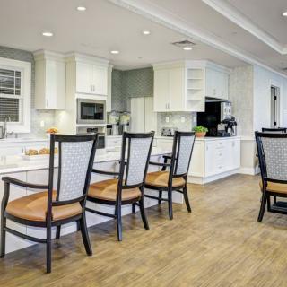 A modern kitchen with white cabinets and a wooden floor featuring an island countertop and dining chairs.