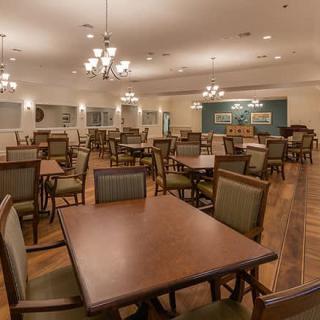 An empty dining room with neatly arranged tables and chairs, featuring elegant lighting and wood flooring.
