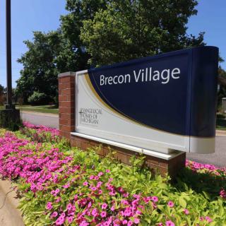 Entrance sign for Brecon Village surrounded by vibrant flowers.