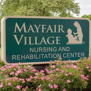Sign for Mayfair Village Nursing and Rehabilitation Center surrounded by flowers.