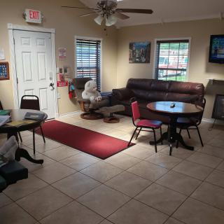 A cozy waiting area with tables, chairs, a sofa, and a ceiling fan on a tiled floor.