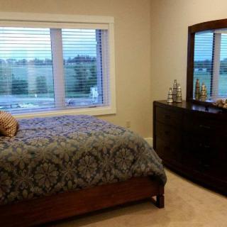 A cozy bedroom featuring a bed with a patterned blanket, a dresser with a mirror, and a window overlooking an outdoor view.