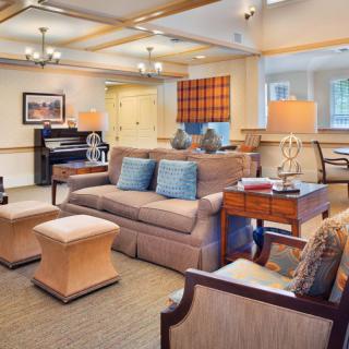 A cozy and elegantly decorated living room featuring a sofa, chairs, coffee table, lamps, and a piano.