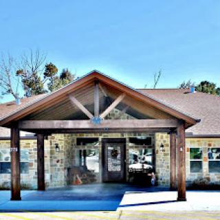 A welcoming entrance featuring a wooden awning and stone facade against a clear blue sky.