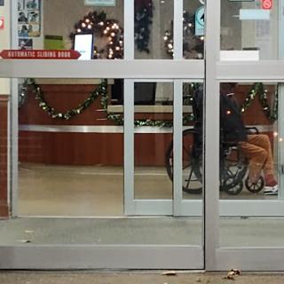 A view of a shopping center entrance, adorned with holiday decorations, featuring a person in a wheelchair.
