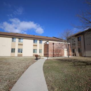 A two-story residential building with a pathway leading to the entrance under a clear blue sky.
