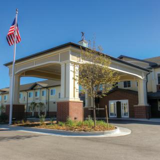 A modern building entrance with an American flag flying nearby under a clear blue sky.