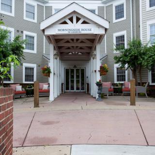 The entrance of a hotel featuring a covered porch and surrounding greenery.