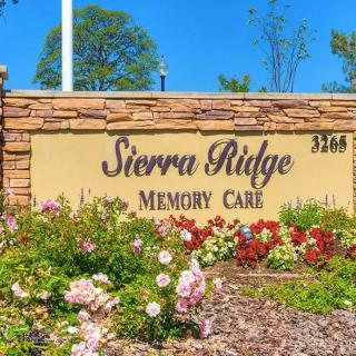 Entrance sign for Sierra Ridge Memory Care with landscaped flowers and a stone wall.