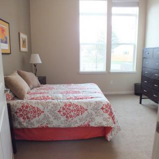 A cozy bedroom with a bed, dresser, and large windows.