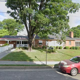 A suburban house with a large tree in the front yard and a car parked on the street.