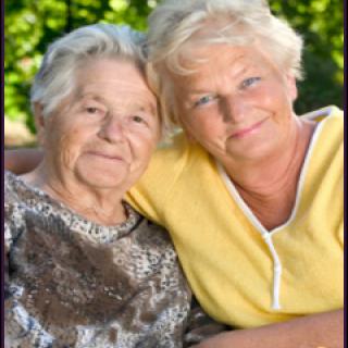 Two elderly women smiling and embracing each other outdoors.