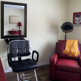 A cozy hair salon corner with a styling chair, mirror, and a vintage hair dryer next to a red sofa.