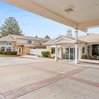 The image shows the entrance of a modern building with a covered driveway and surrounding landscaping.