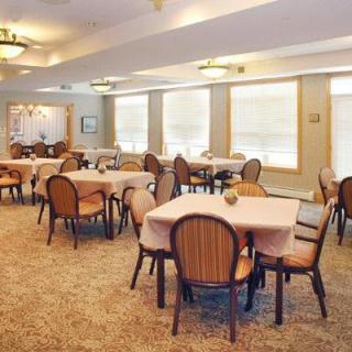 A spacious dining room with multiple tables and chairs, featuring elegant lighting and carpeted floors.