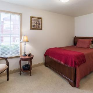 A cozy bedroom with a single bed, a bedside table, and a lamp by the window.