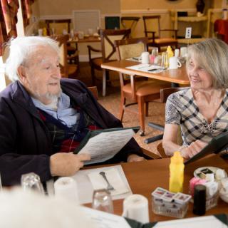 An elderly man and a woman are having a conversation in a restaurant while looking at the menu.
