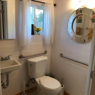 A small bathroom with a toilet, sink, mirror, and grab bars.