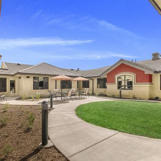 A residential building with a landscaped yard and patio under a clear blue sky.