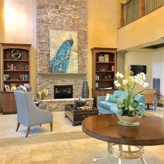 A stylish living room with a high ceiling, featuring a prominent fireplace, elegant furniture, and artistic decor.