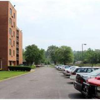 A parking lot beside a multi-story building with several parked cars and trees in the background.