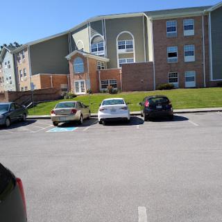 A view of an apartment building with parked cars in the foreground on a sunny day.