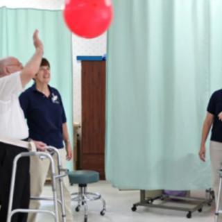 An elderly person engaging in a ball exercise during a physical therapy session with healthcare professionals.