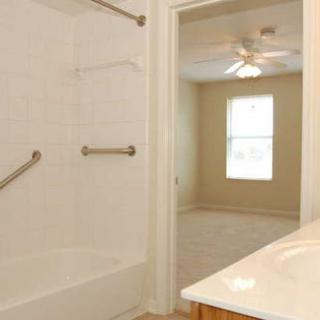 A spacious and bright bathroom with a bathtub, shower, and adjacent room featuring a ceiling fan.