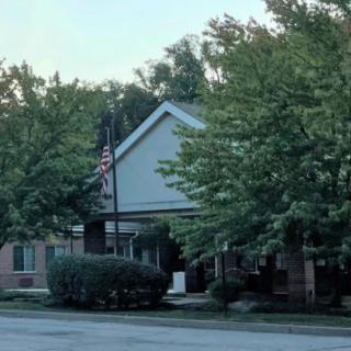 A suburban building partially obscured by trees, with a flagpole visible in front.