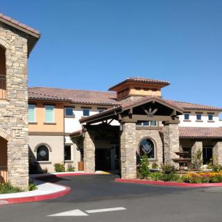 A stone-facade building with a welcoming entrance and well-maintained landscaping on a sunny day.