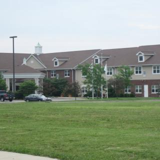 A large building with a grassy lawn and cars parked nearby.