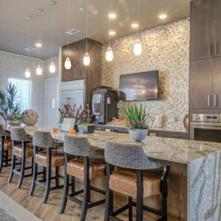 Modern kitchen interior with a stylish counter and bar stools, adorned with pendant lighting and decorative plants.