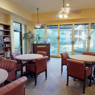 A cozy seating area with tables and chairs, surrounded by bookshelves and large windows allowing natural light to fill the room.