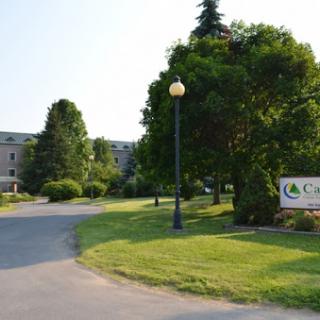 A scenic view of a pathway leading to a building, surrounded by greenery and a welcoming sign.