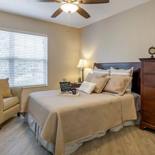 A cozy bedroom with a neatly made bed, a ceiling fan, and warm lighting.