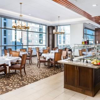 A spacious and elegantly designed dining area with large windows, wooden furniture, and a buffet setup.