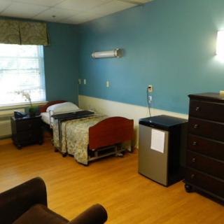 A simple hospital room with a bed, dresser, and small refrigerator.
