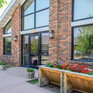 A brick building with large windows and a planter filled with colorful flowers at the entrance.