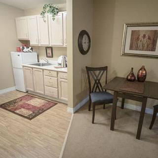 A compact apartment kitchen with adjacent dining area, featuring beige cabinets, a small table, and decorative elements.