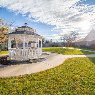 A picturesque gazebo in a sunny garden setting surrounded by green grass and a winding pathway.