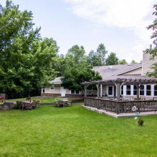 A backyard view of a house with a spacious lawn and a wooden deck surrounded by trees.