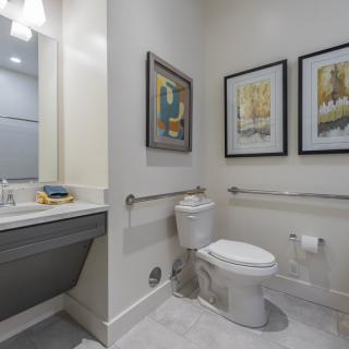A modern bathroom featuring a toilet, sink with mirror, and framed wall art.